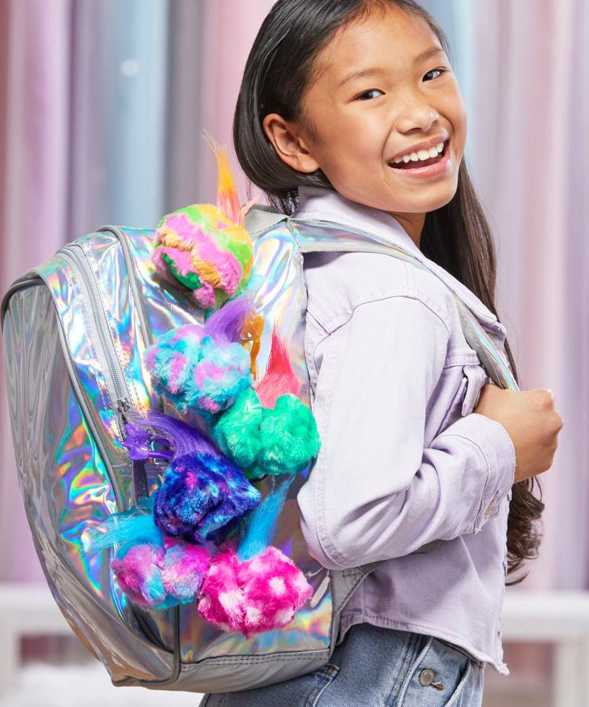 Child with a colorful backpack featuring pom-poms against a light curtain background